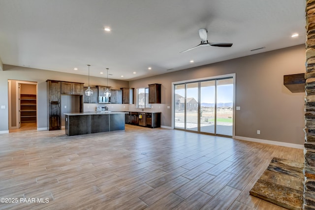 kitchen with a ceiling fan, a kitchen island, open floor plan, light countertops, and wood tiled floor