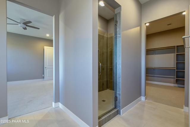 bathroom featuring a stall shower, baseboards, a walk in closet, and ceiling fan