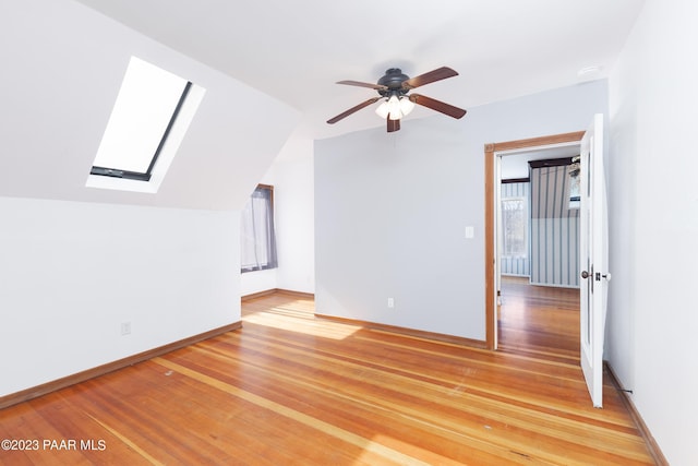 additional living space featuring wood-type flooring, ceiling fan, and vaulted ceiling with skylight