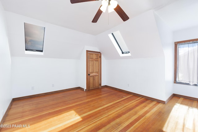 bonus room with hardwood / wood-style flooring, lofted ceiling with skylight, and ceiling fan