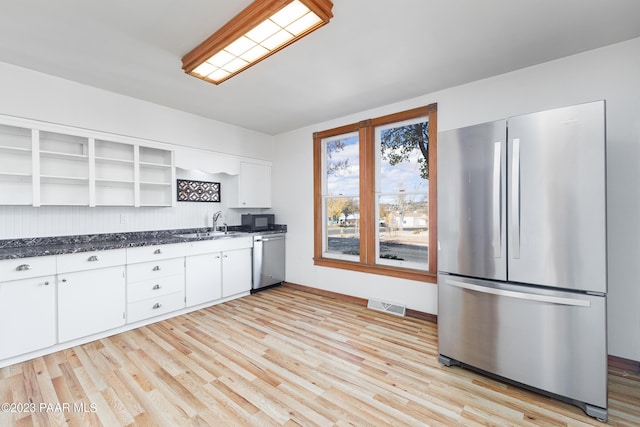 kitchen with dark stone counters, stainless steel appliances, sink, light hardwood / wood-style flooring, and white cabinetry