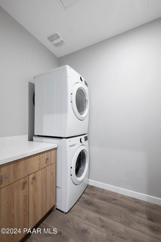 clothes washing area with cabinets, dark hardwood / wood-style flooring, and stacked washing maching and dryer