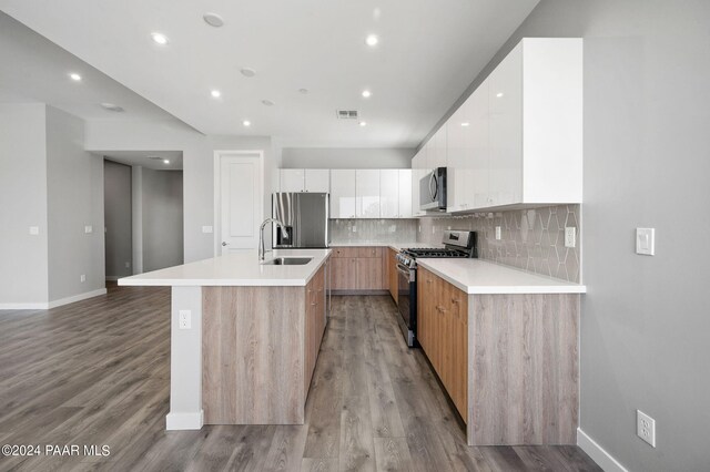 kitchen featuring a kitchen island with sink, sink, light wood-type flooring, appliances with stainless steel finishes, and white cabinetry