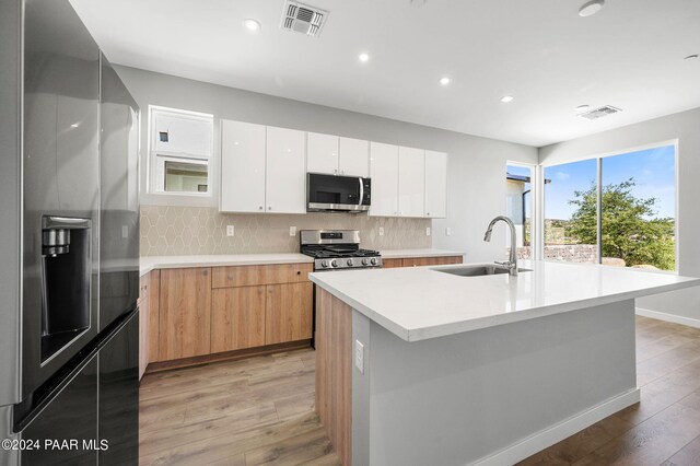 kitchen with sink, appliances with stainless steel finishes, a kitchen island with sink, white cabinets, and light wood-type flooring