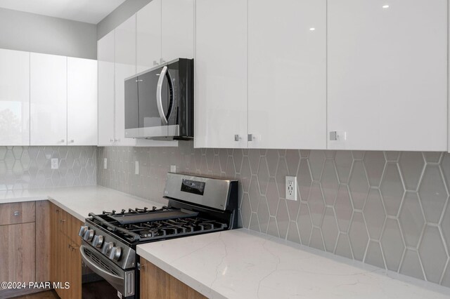 kitchen with backsplash, white cabinetry, light stone countertops, and appliances with stainless steel finishes