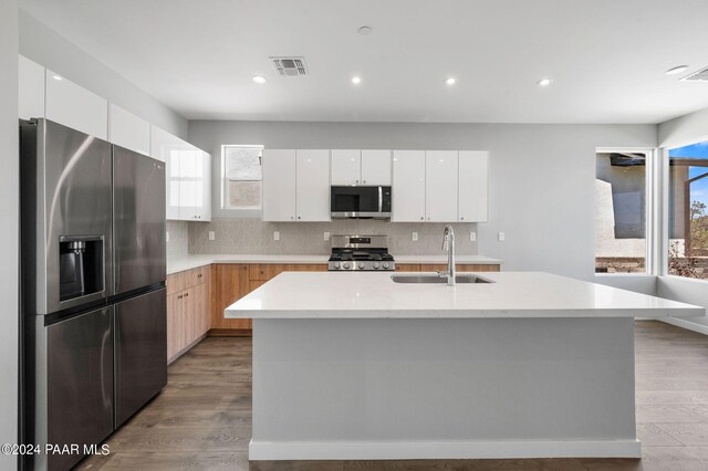 kitchen with appliances with stainless steel finishes, light wood-type flooring, a kitchen island with sink, sink, and white cabinetry