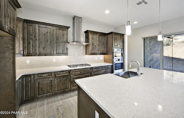 kitchen featuring wall chimney exhaust hood, a sink, visible vents, dark brown cabinetry, and appliances with stainless steel finishes