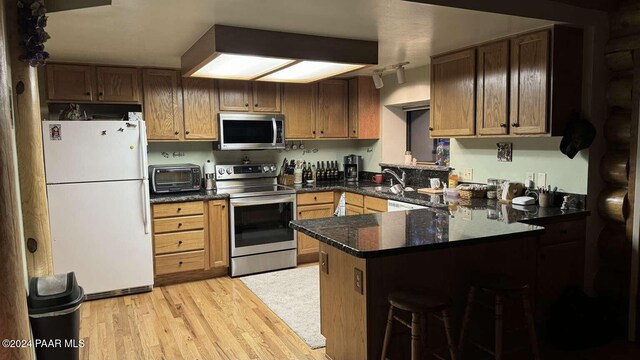 kitchen featuring kitchen peninsula, a kitchen bar, light wood-type flooring, stainless steel appliances, and sink