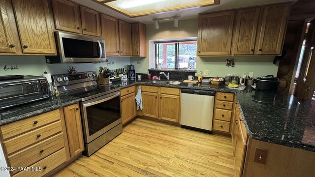 kitchen featuring dark stone counters, sink, light hardwood / wood-style floors, and appliances with stainless steel finishes