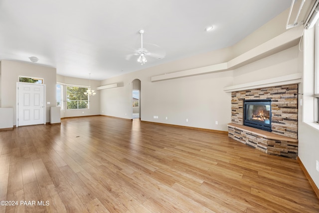 unfurnished living room with light hardwood / wood-style floors, a stone fireplace, ceiling fan, and a wall unit AC