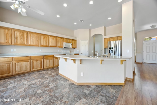 kitchen featuring dark hardwood / wood-style flooring, white appliances, ceiling fan, sink, and a breakfast bar area