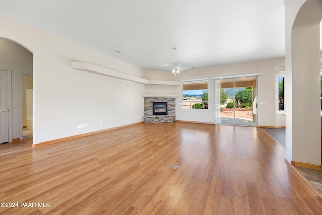 unfurnished living room featuring light hardwood / wood-style flooring, ceiling fan, and a stone fireplace