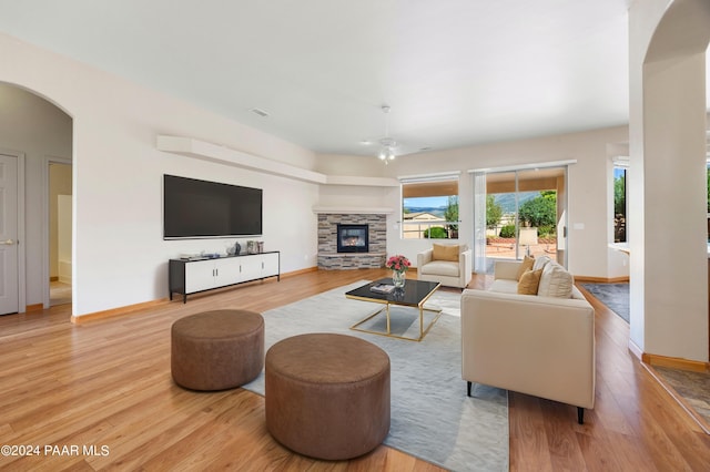 living room featuring light hardwood / wood-style floors, a stone fireplace, and ceiling fan