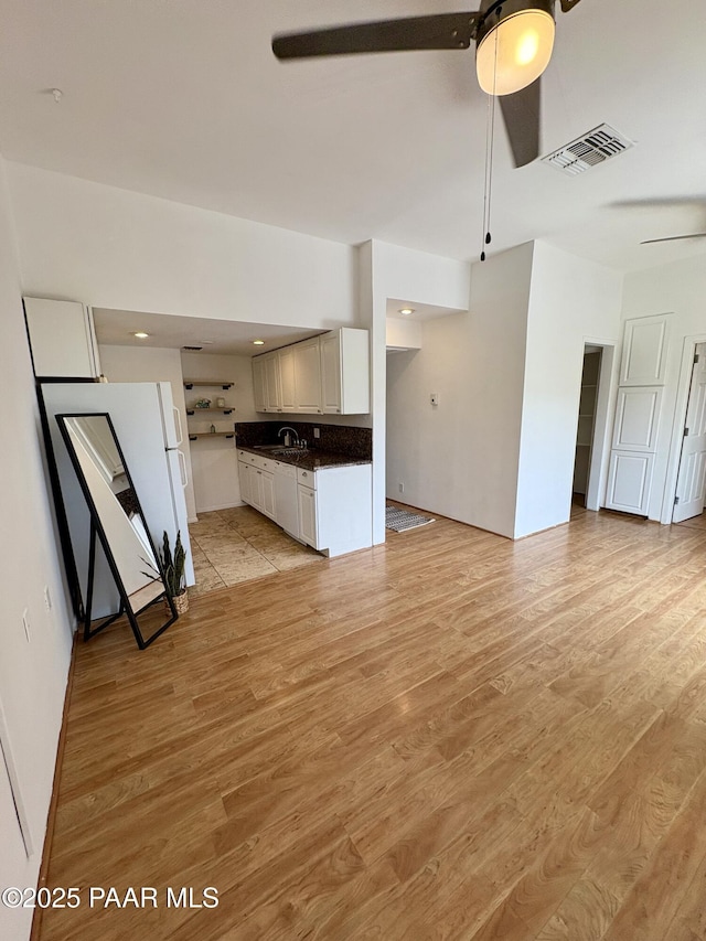 unfurnished living room featuring ceiling fan, light wood-style flooring, visible vents, and a sink
