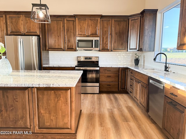 kitchen featuring sink, hanging light fixtures, stainless steel appliances, light stone countertops, and light hardwood / wood-style floors