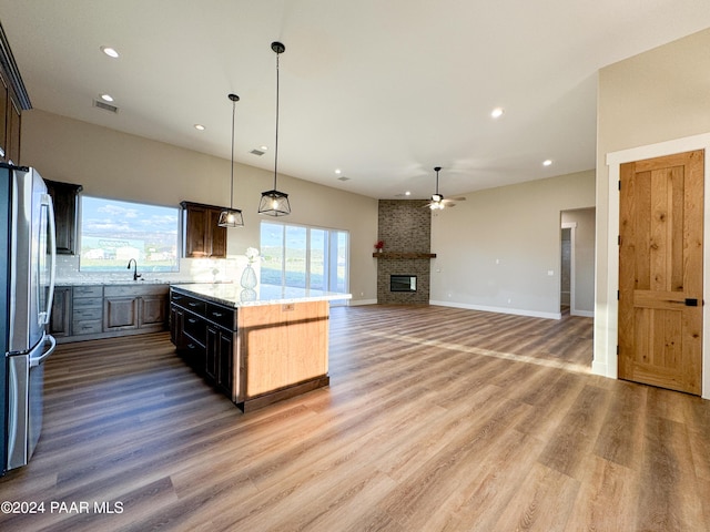 kitchen with a kitchen island, stainless steel refrigerator, a large fireplace, hanging light fixtures, and light stone counters