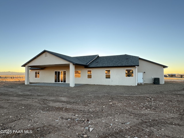 back house at dusk with central AC unit and a patio