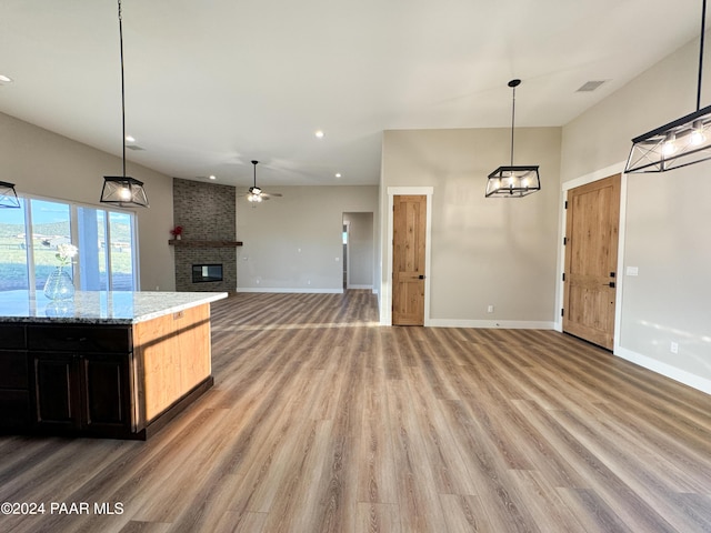 kitchen featuring pendant lighting, a brick fireplace, ceiling fan, light stone countertops, and light hardwood / wood-style flooring