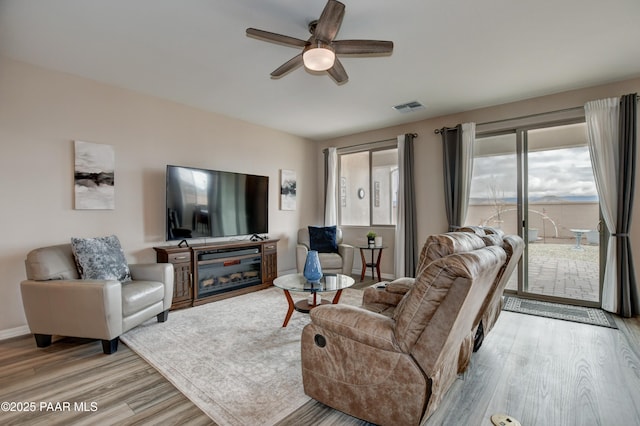 living room featuring a ceiling fan, visible vents, light wood finished floors, and baseboards