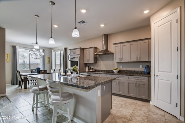 kitchen with a sink, a kitchen island with sink, wall chimney exhaust hood, and gray cabinets