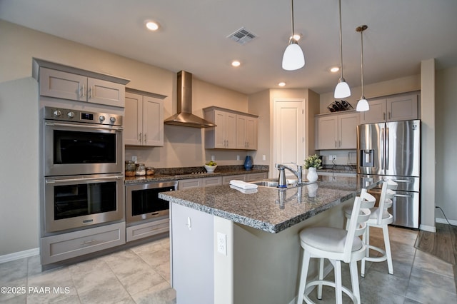 kitchen featuring visible vents, a sink, gray cabinetry, appliances with stainless steel finishes, and wall chimney range hood