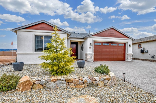 view of front facade featuring decorative driveway, stone siding, an attached garage, and stucco siding