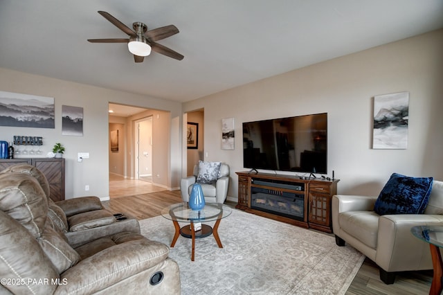 living area with baseboards, ceiling fan, and wood finished floors