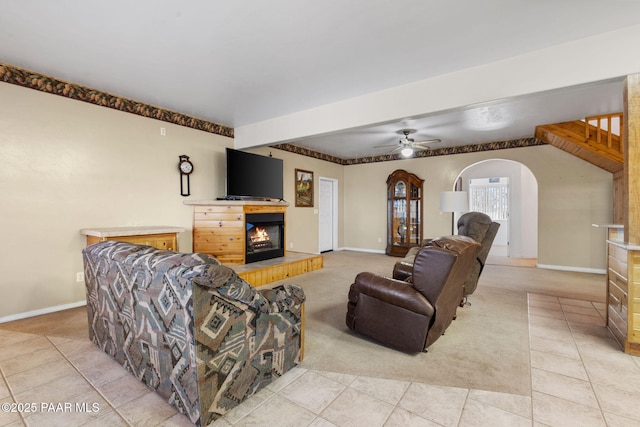 living area featuring light tile patterned flooring, ceiling fan, arched walkways, a glass covered fireplace, and light colored carpet