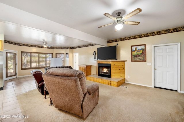 living room with a warm lit fireplace, baseboards, ceiling fan, tile patterned floors, and carpet floors
