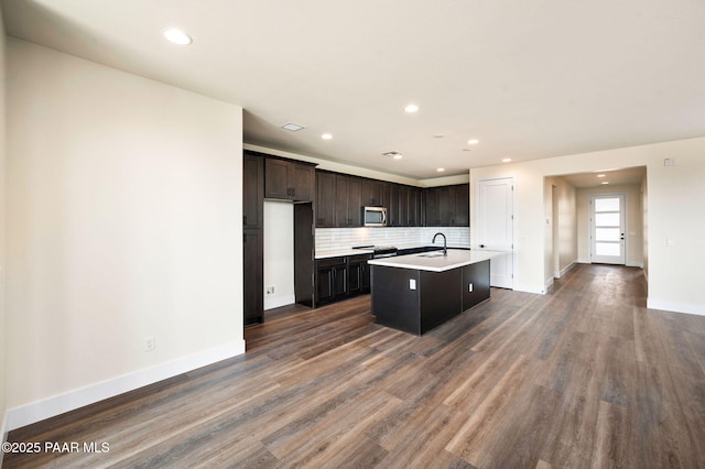 kitchen with a kitchen island with sink, sink, decorative backsplash, dark brown cabinets, and stainless steel appliances