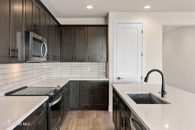 kitchen with light stone countertops, sink, stainless steel appliances, backsplash, and light wood-type flooring