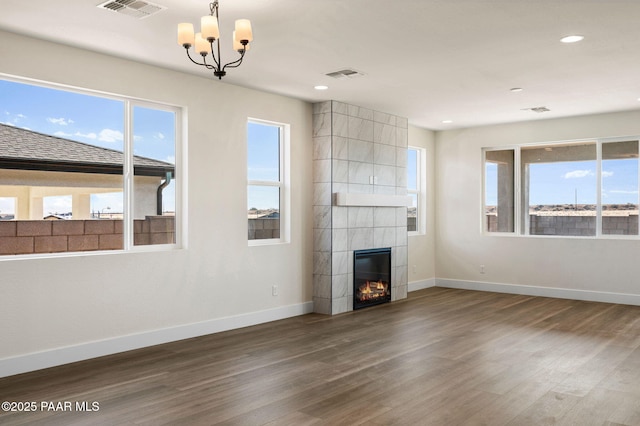 unfurnished living room featuring a wealth of natural light, a fireplace, a chandelier, and hardwood / wood-style flooring