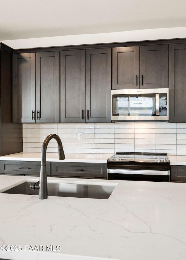 kitchen featuring sink, dark brown cabinets, light stone countertops, and appliances with stainless steel finishes