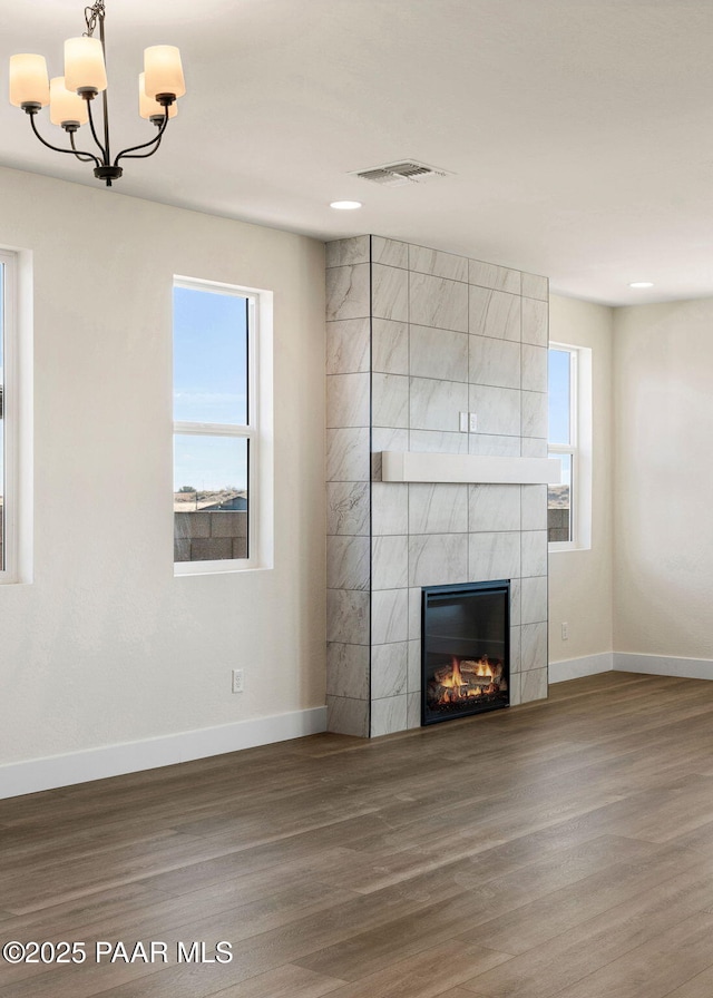 unfurnished living room with hardwood / wood-style flooring, a wealth of natural light, a notable chandelier, and a tiled fireplace