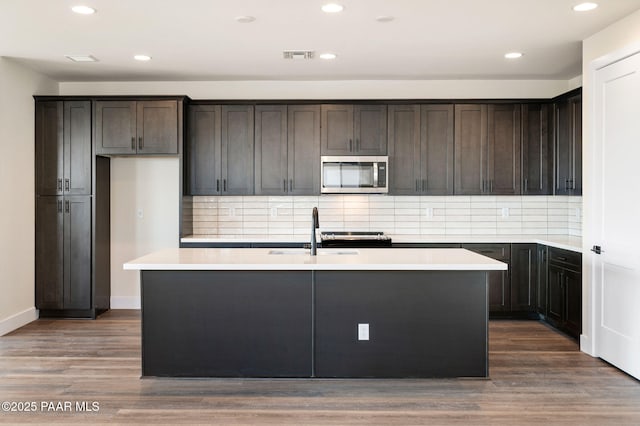 kitchen with a center island with sink, backsplash, wood-type flooring, and sink