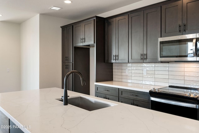 kitchen with dark brown cabinets, electric range oven, light stone counters, and sink