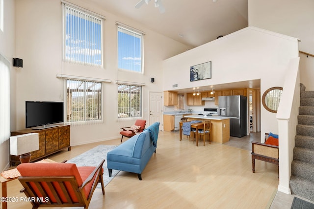 living room with stairway, a ceiling fan, light wood-style floors, and a towering ceiling