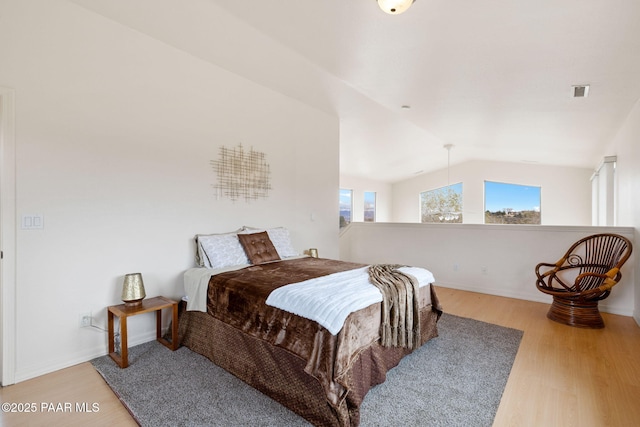 bedroom with lofted ceiling, wood finished floors, visible vents, and baseboards