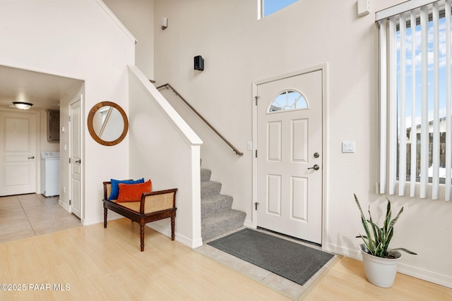 entryway featuring a towering ceiling, baseboards, wood finished floors, and stairs