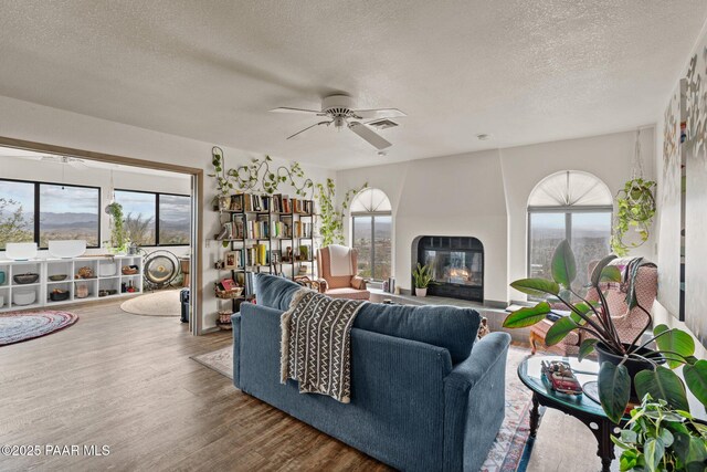 969 S Saguaro Dr, Wickenburg, AZ 85390 - living room featuring a textured ceiling, a glass covered fireplace, ceiling fan, and wood finished floors