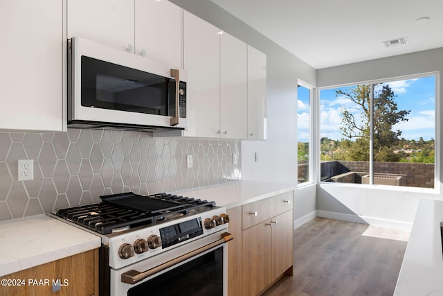 kitchen featuring visible vents, gas range, white microwave, wood finished floors, and decorative backsplash