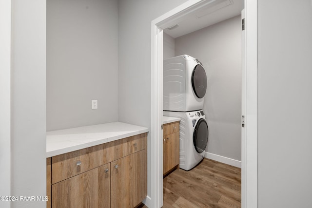 clothes washing area with stacked washer / dryer, light wood finished floors, baseboards, and cabinet space