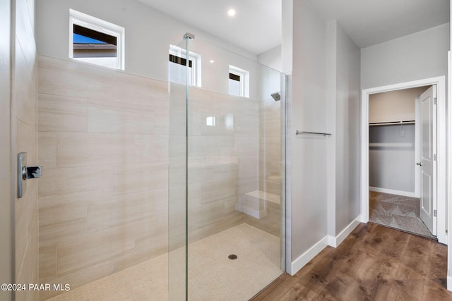 full bathroom featuring wood finished floors, baseboards, a spacious closet, and walk in shower