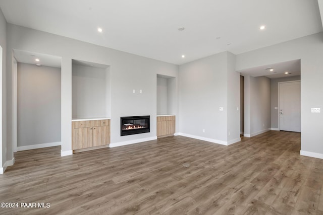 unfurnished living room with light wood finished floors, baseboards, a glass covered fireplace, and recessed lighting