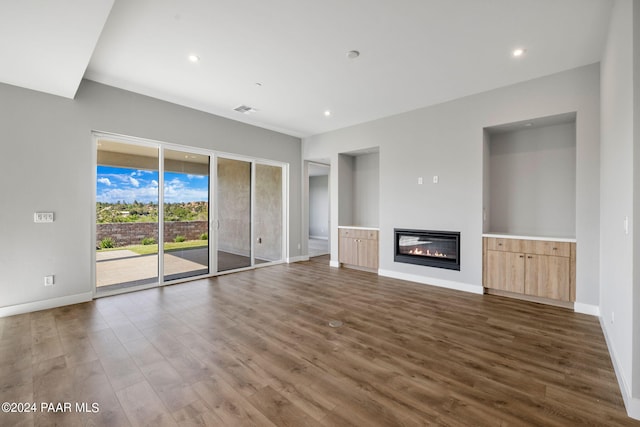 unfurnished living room featuring dark wood finished floors, a glass covered fireplace, visible vents, recessed lighting, and baseboards