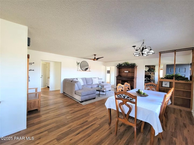 dining area featuring ceiling fan with notable chandelier, a fireplace, a textured ceiling, and wood finished floors