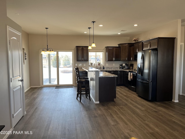 kitchen featuring dark brown cabinets, a center island, black appliances, a kitchen bar, and decorative light fixtures