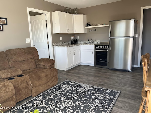 kitchen featuring high end black range oven, white cabinetry, stainless steel fridge, dark hardwood / wood-style flooring, and light stone countertops