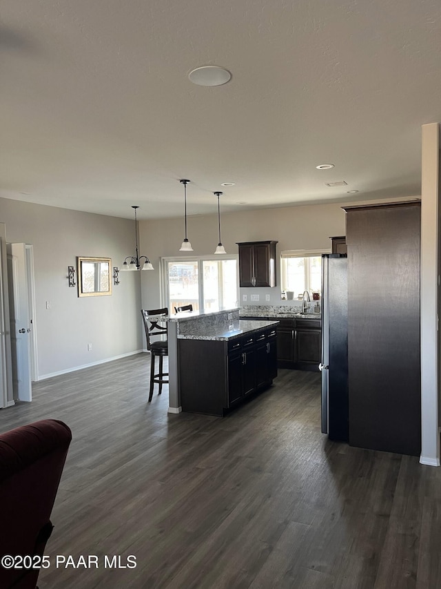 kitchen with pendant lighting, sink, stainless steel refrigerator, dark brown cabinets, and a kitchen island