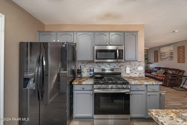 kitchen with gray cabinetry, light stone countertops, appliances with stainless steel finishes, and tasteful backsplash